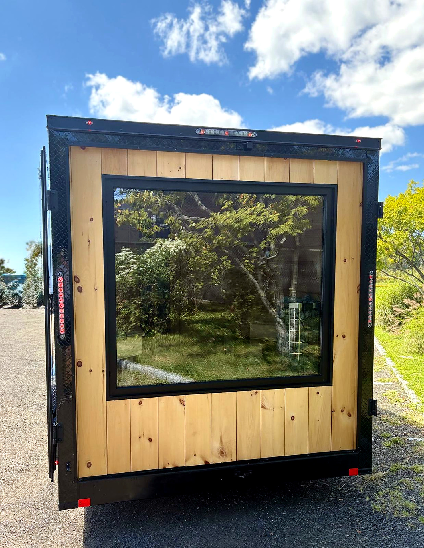 Rear exterior of the mobile sauna trailer with a large picture window framed in cedar